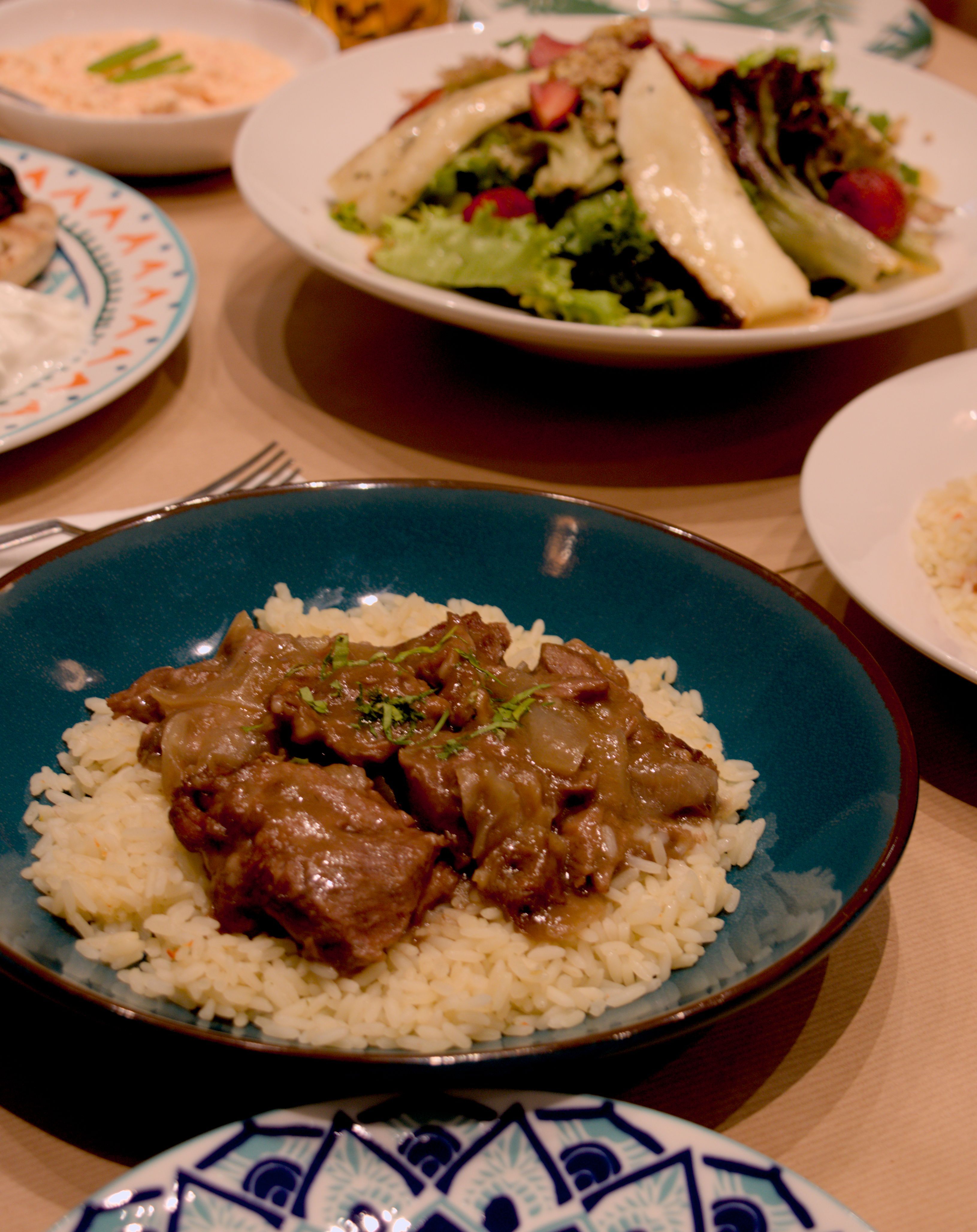 Close up, eye level view of a plate with chunks of meat on a bed of rice. Other plates are in the background, blurred